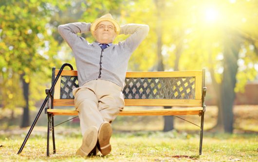 homme aîné, à, canne, séance banc, dans parc, à, coucher soleil