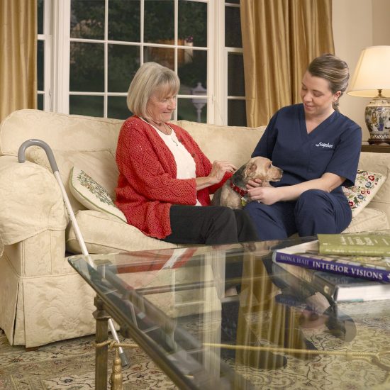 senior woman and caregiver petting dog at home