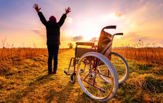 Homme debout avec les bras tendus à côté d'un fauteuil roulant vide