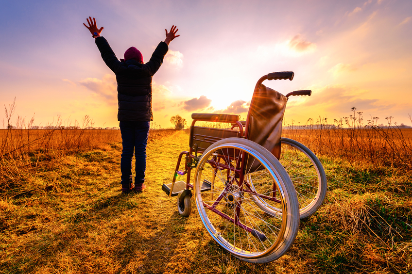 Homme debout avec les bras tendus à côté d'un fauteuil roulant vide