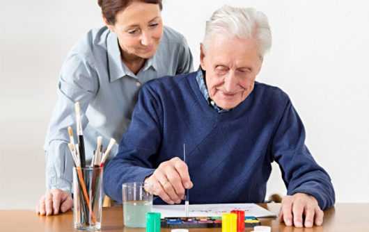 senior man painting with woman looking over his shoulder