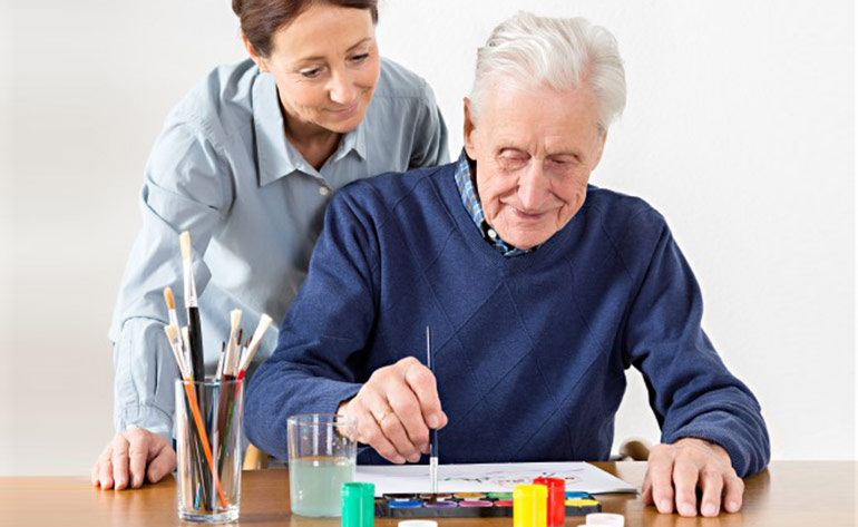 senior man painting with woman looking over his shoulder