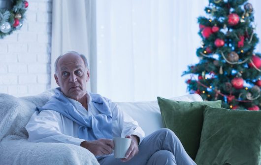 Senior man sitting alone by Christmas tree