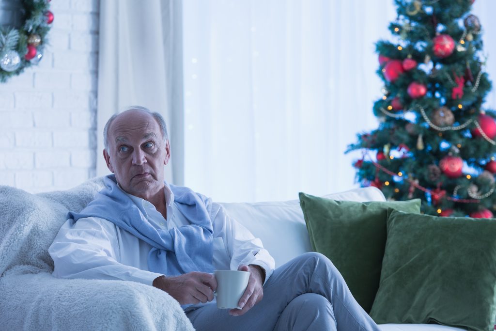 Senior man sitting alone by Christmas tree