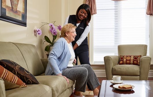 Caregiver helping woman stand up from couch