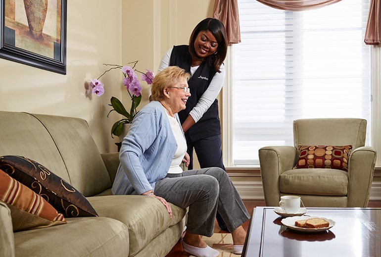 Caregiver helping woman stand up from couch