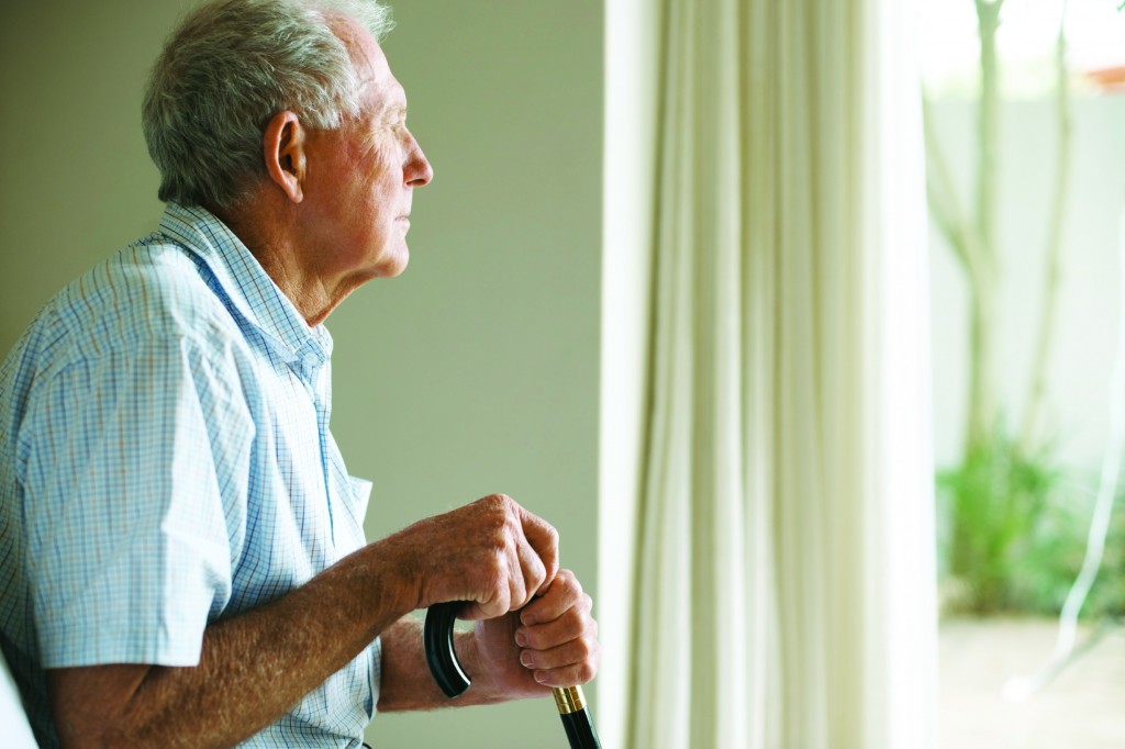 Senior man holding cane and looking out of window