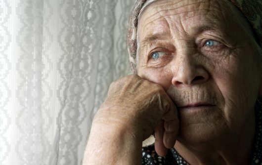 femme senior regardant par la fenêtre malheureusement