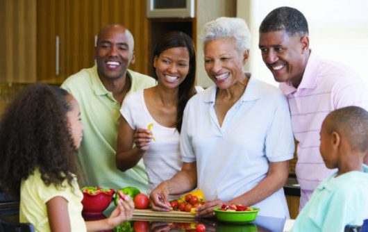 famille multigénérationnelle mangeant des légumes dans la cuisine et souriant