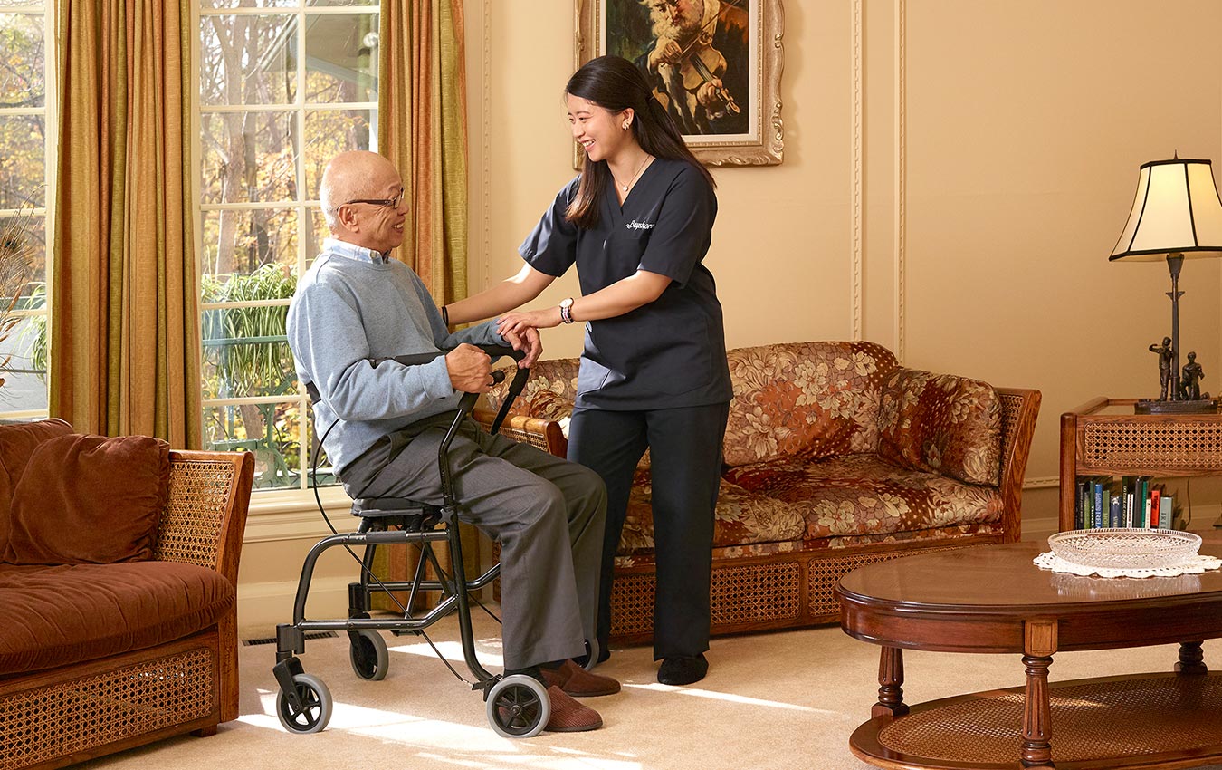 Senior man sat in a walker while a caregiver is providing assistance. They both are smiling at each other.