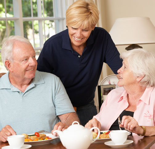soignant souriant à un couple de personnes âgées mangeant à table