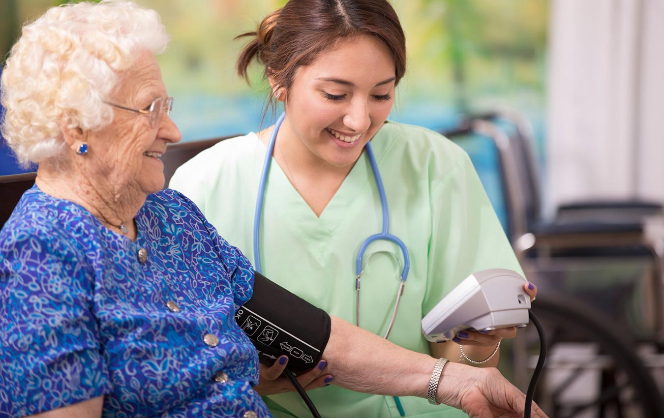 Nurse checking an elderly woman's blood pressure. They both look happy.