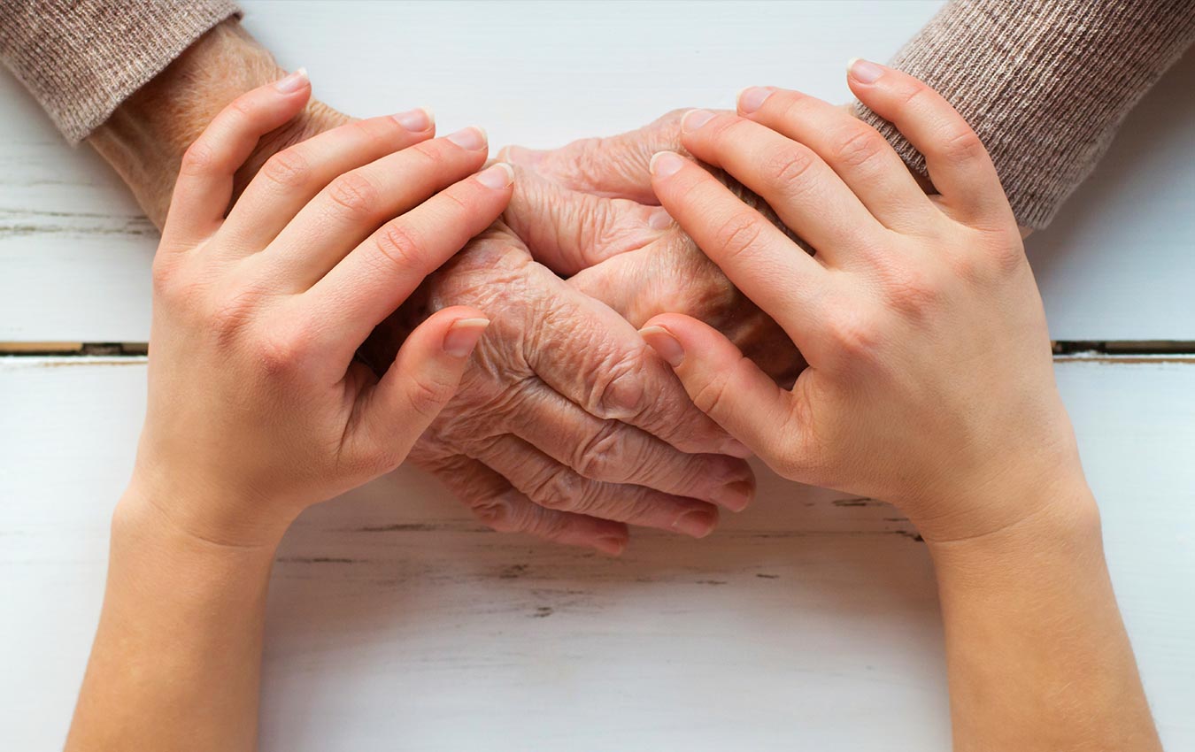 A pair of young hands on top of a pair of old hands showing comfort and care.