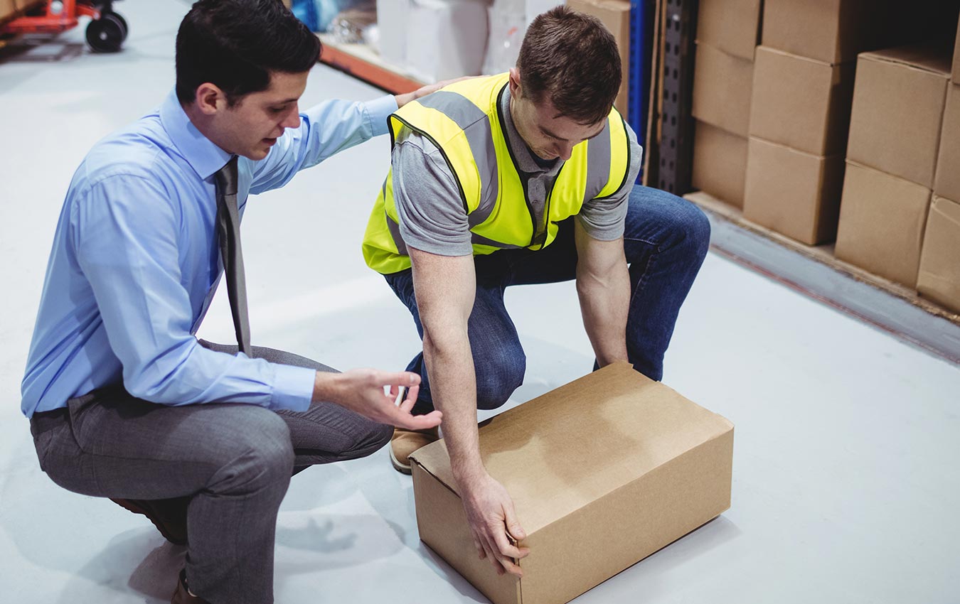 A man is assisting a worker who is picking up a box from the floor.