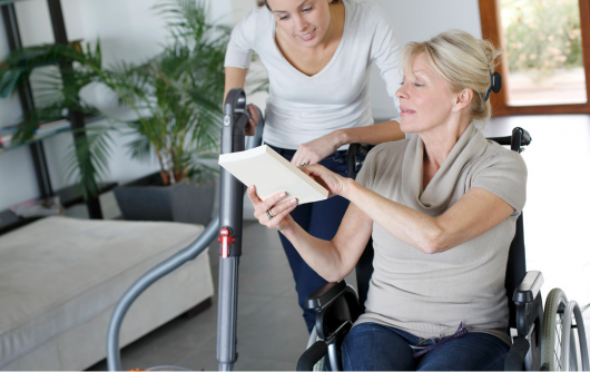 Woman in a wheelchair showing a book to a female nurse.