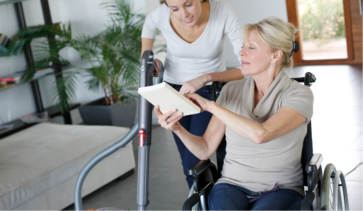 Woman in a wheelchair showing a book to a female nurse.