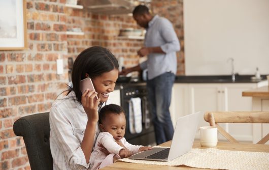 Mère et bébé sur ordinateur portable dans la cuisine pendant que le père prépare le dîner