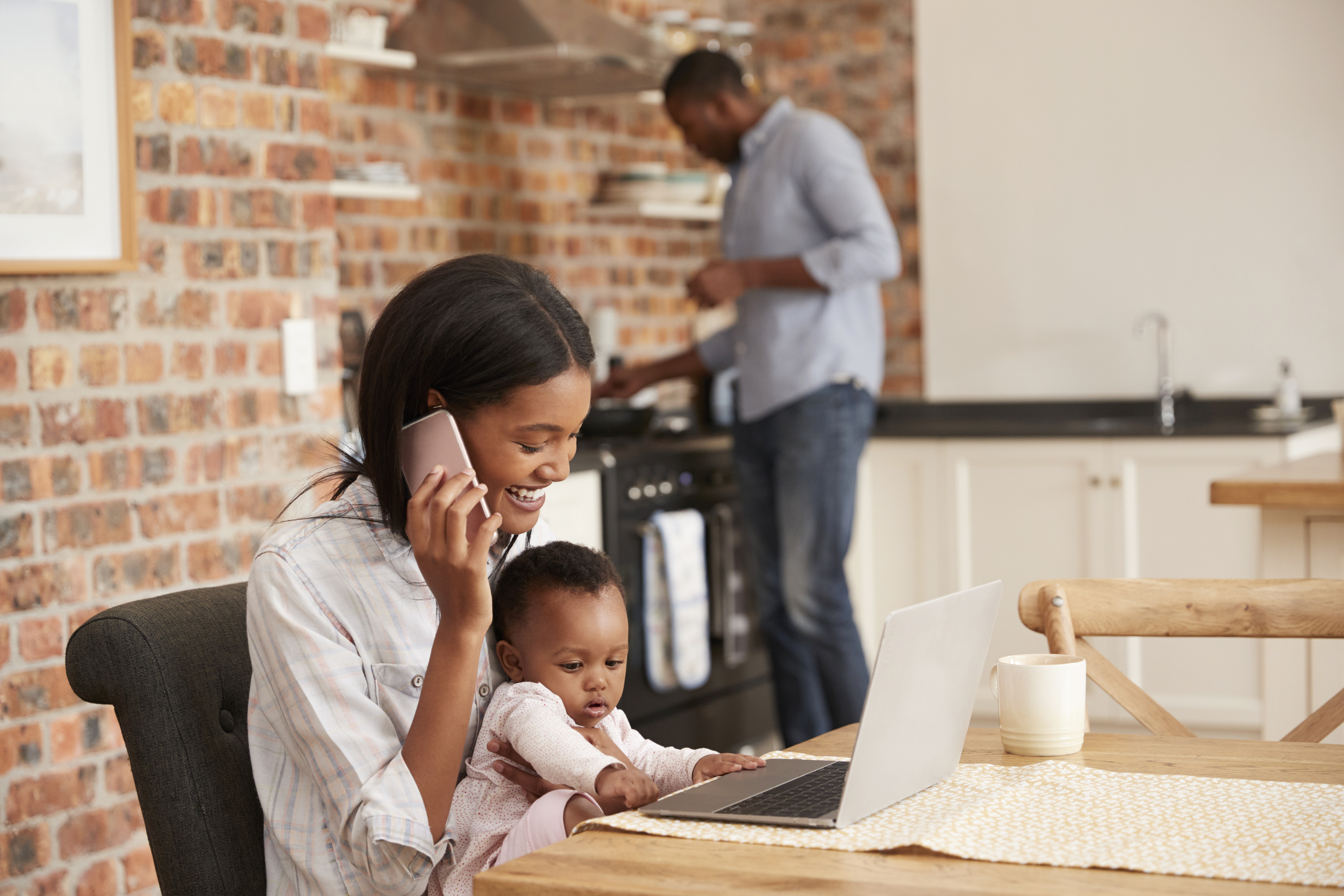 Mère et bébé sur ordinateur portable dans la cuisine pendant que le père prépare le dîner