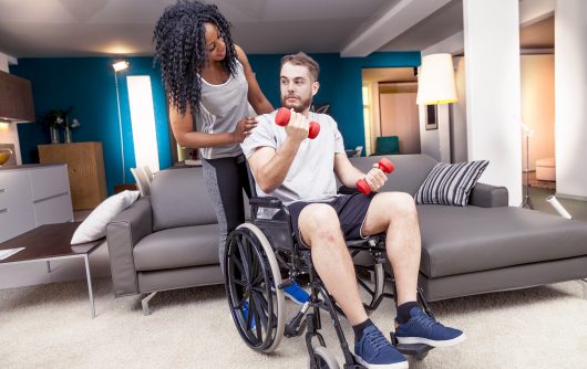 Woman helping man in wheelchair lift weights