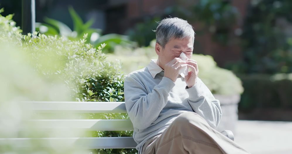 man on park bench sneezing