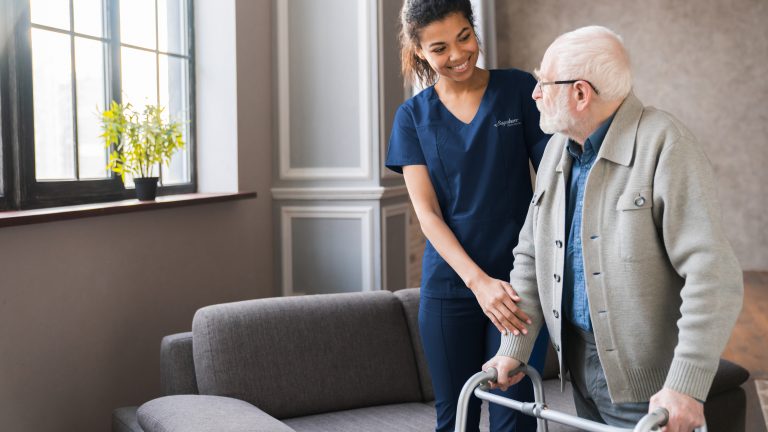 Portrait of an african young nurse helping old elderly disable man grandfather to walk using walker equipment in the bedroom.