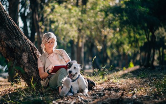 woman sitting in park reading with dog