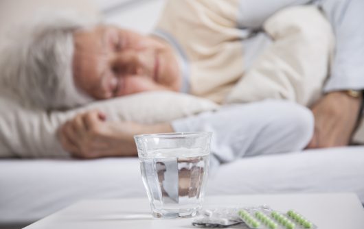 Woman sleeping in bed next to nightstand with pills and water