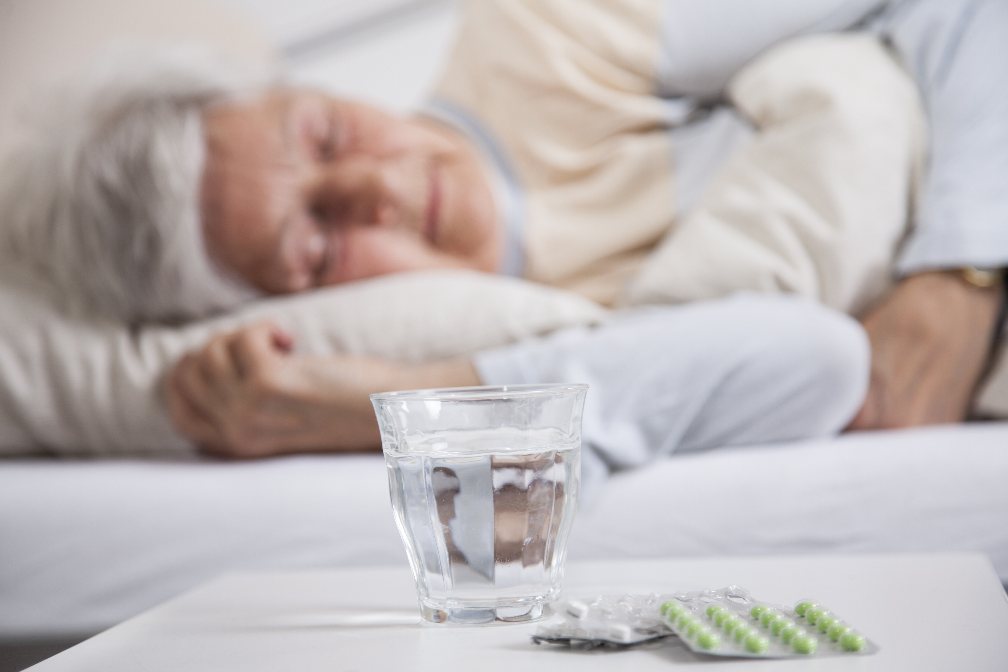 Woman sleeping in bed next to nightstand with pills and water