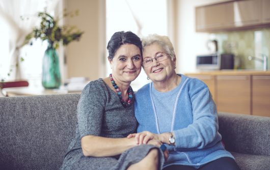 elderly mother and daughter embracing on couch