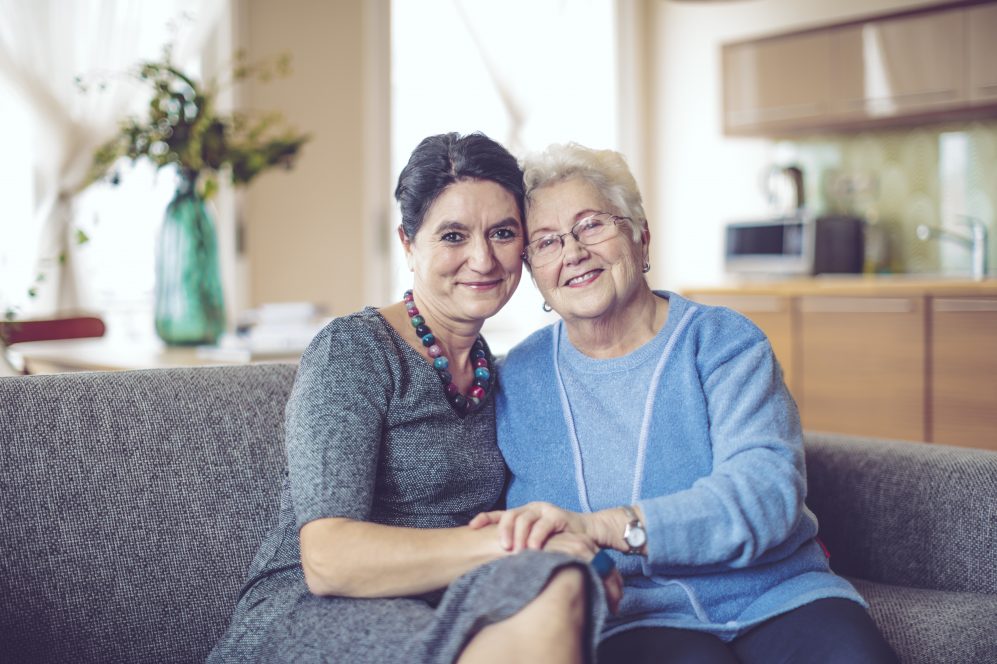 elderly mother and daughter embracing on couch