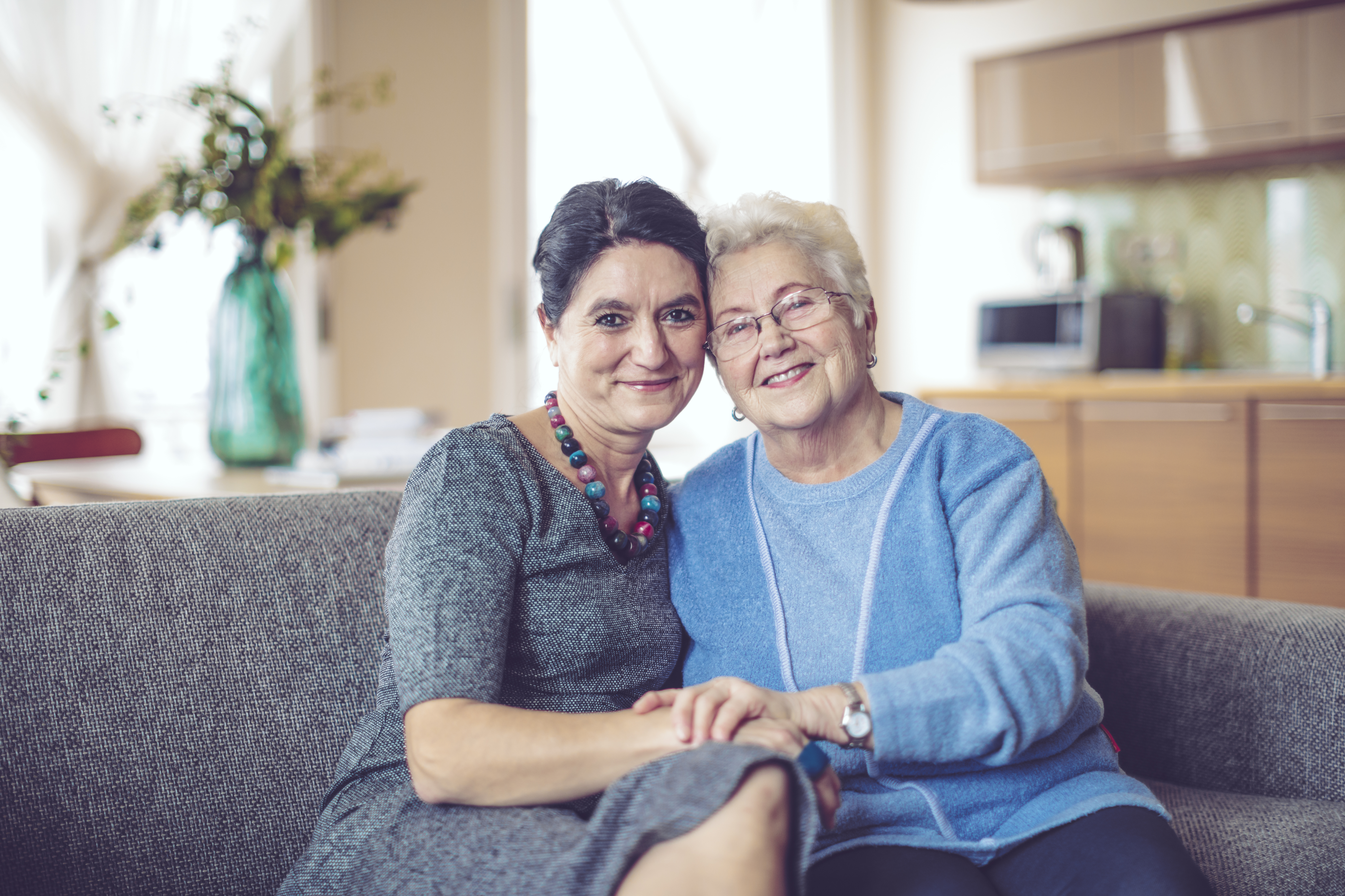 elderly mother and daughter embracing on couch