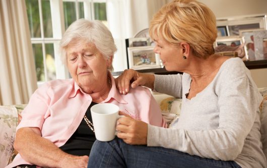 Daughter comforting elderly mother on sofa