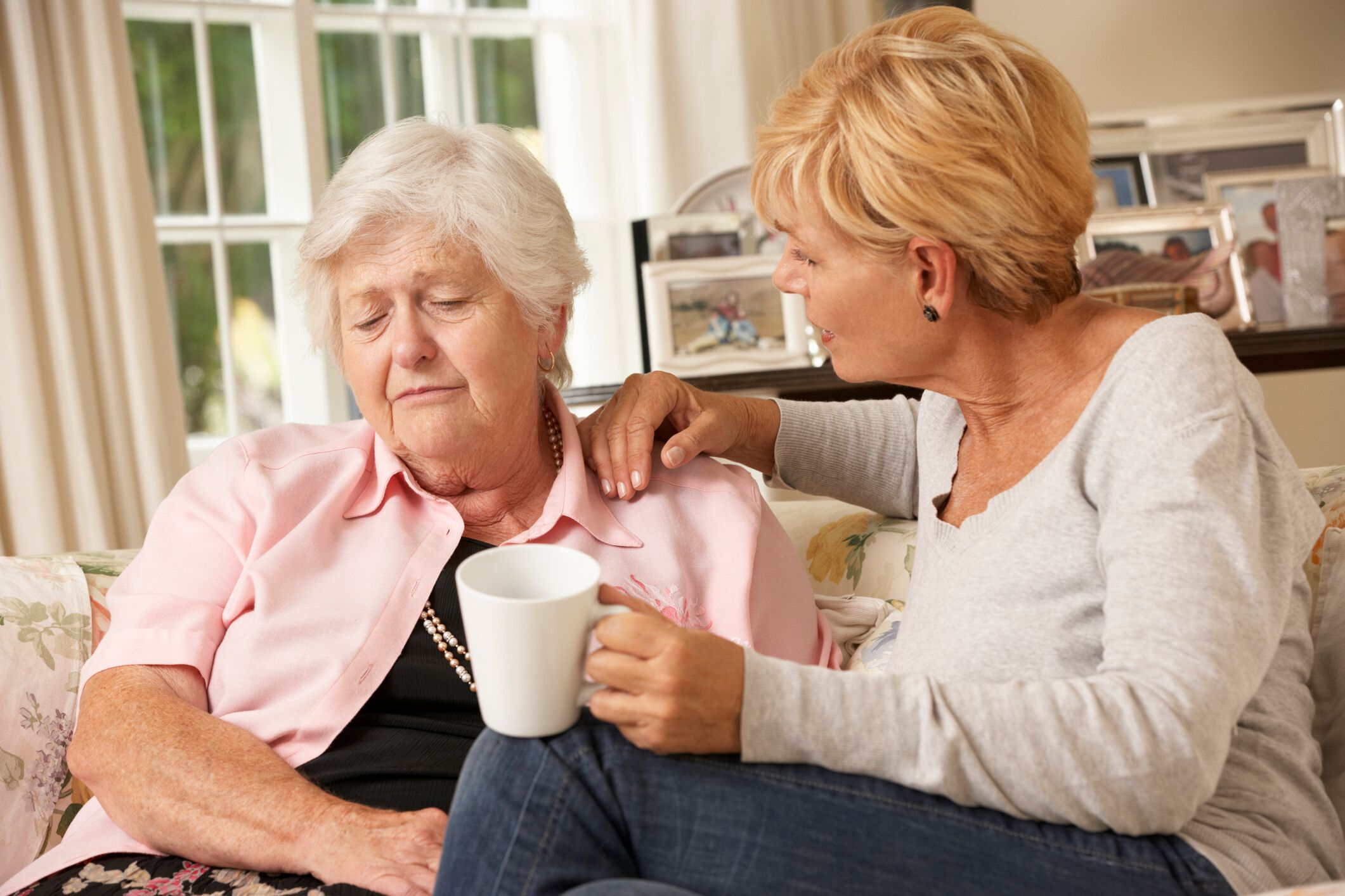 Daughter comforting elderly mother on sofa