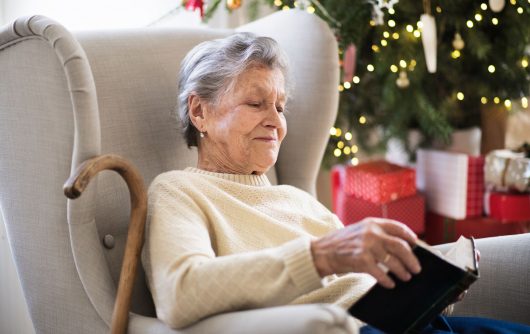 Senior woman sitting on couch avec livre de lecture de canne