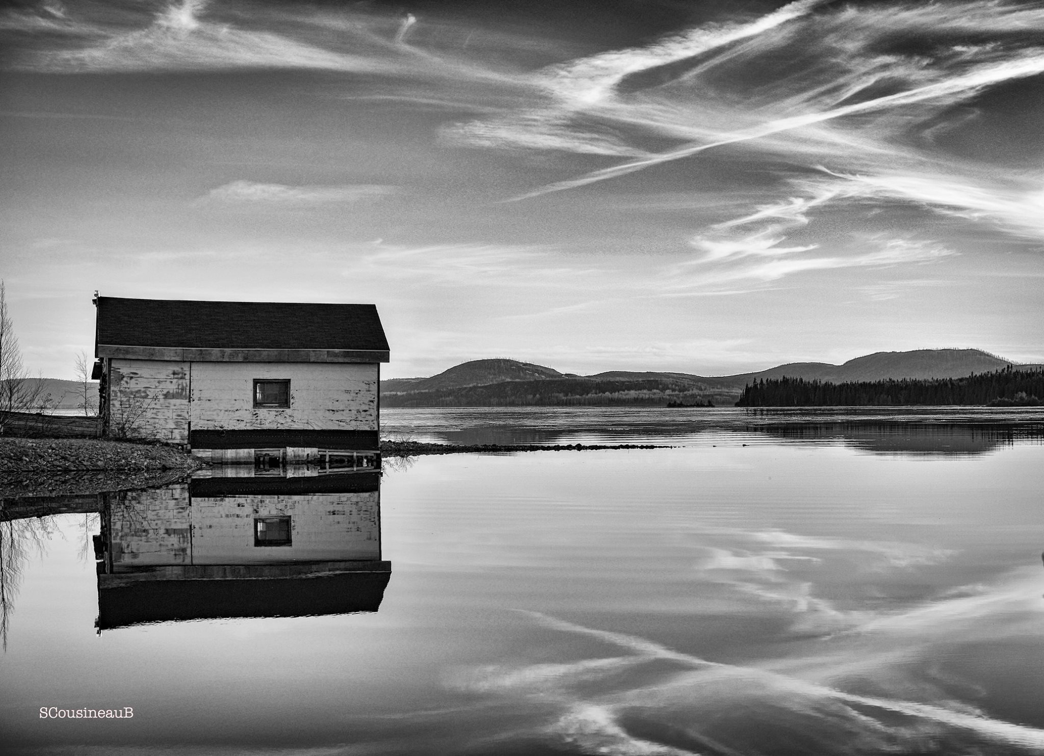 Black and white photo of solitary house on peaceful lake