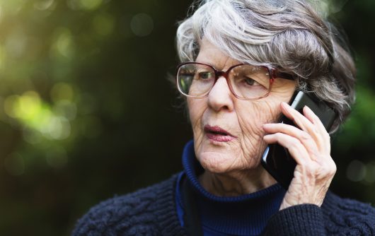 Serious senior woman talking on phone outdoors seems concerned