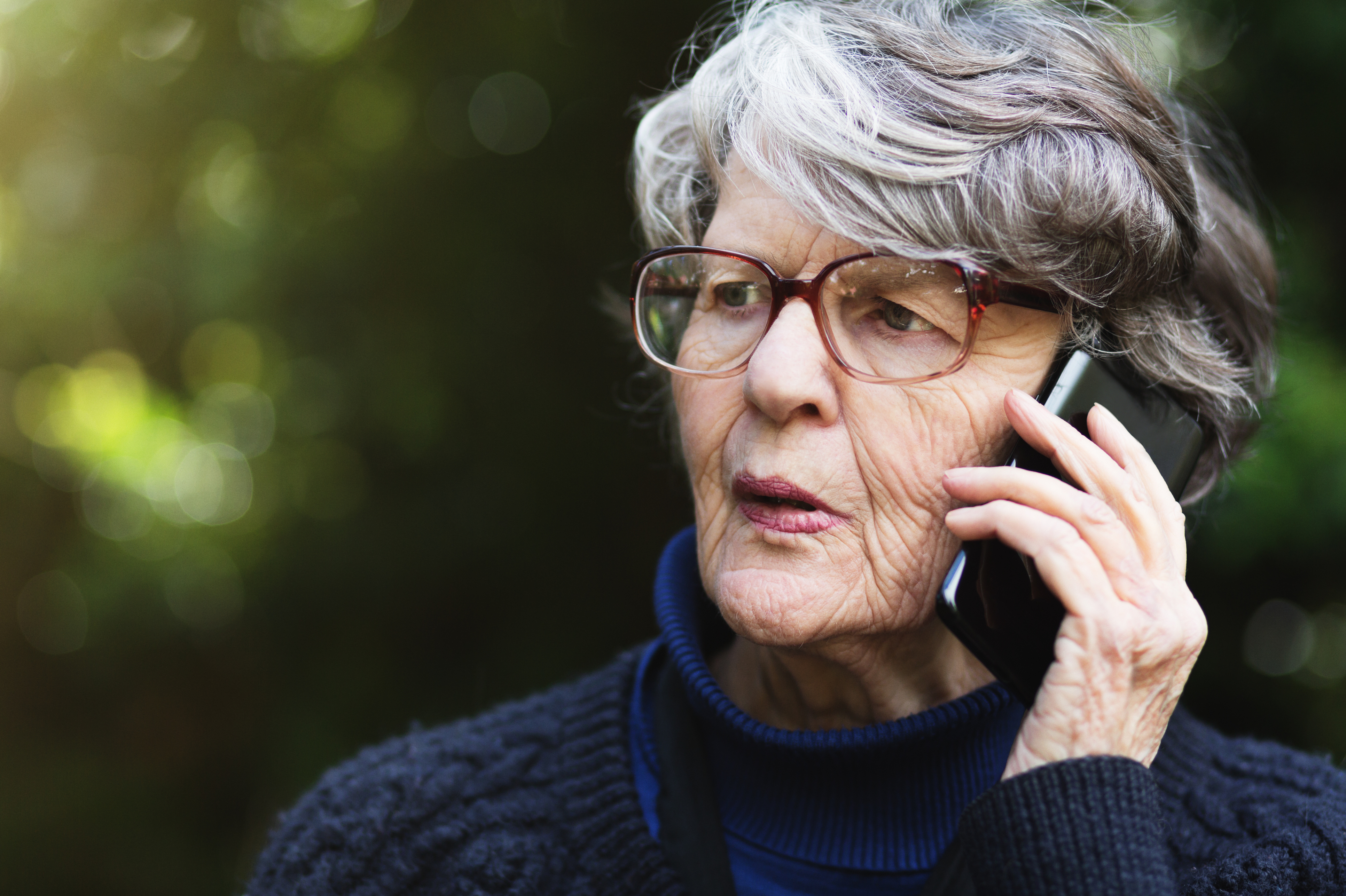 Serious senior woman talking on phone outdoors seems concerned