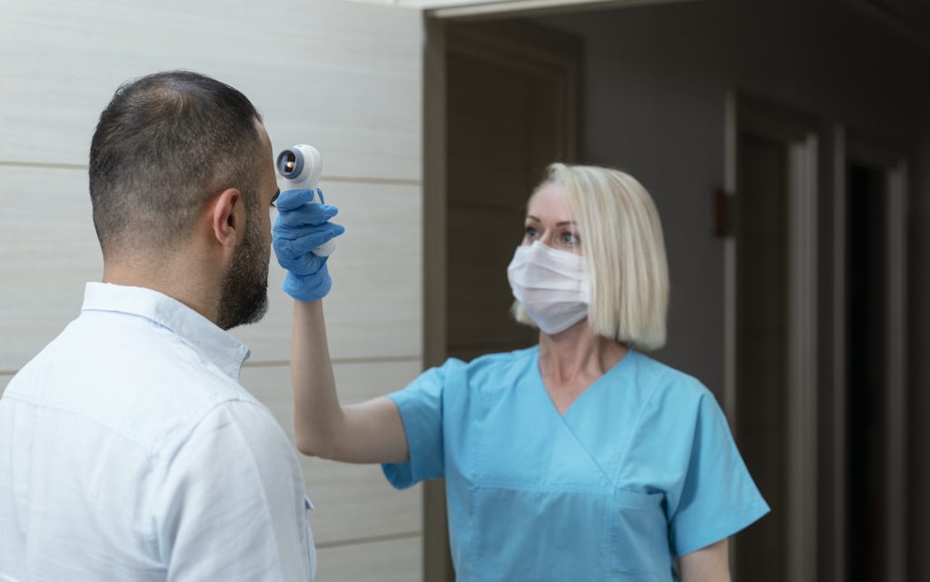 Female doctor checking temperature at patient with infrared tool in hospital