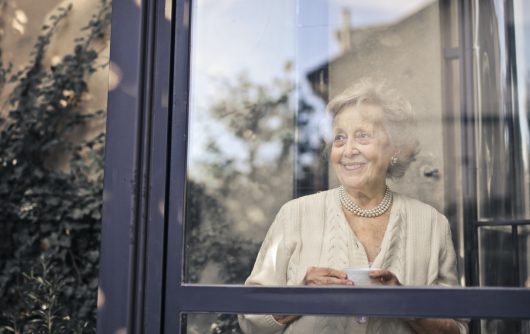senior woman smiling out window holding tea