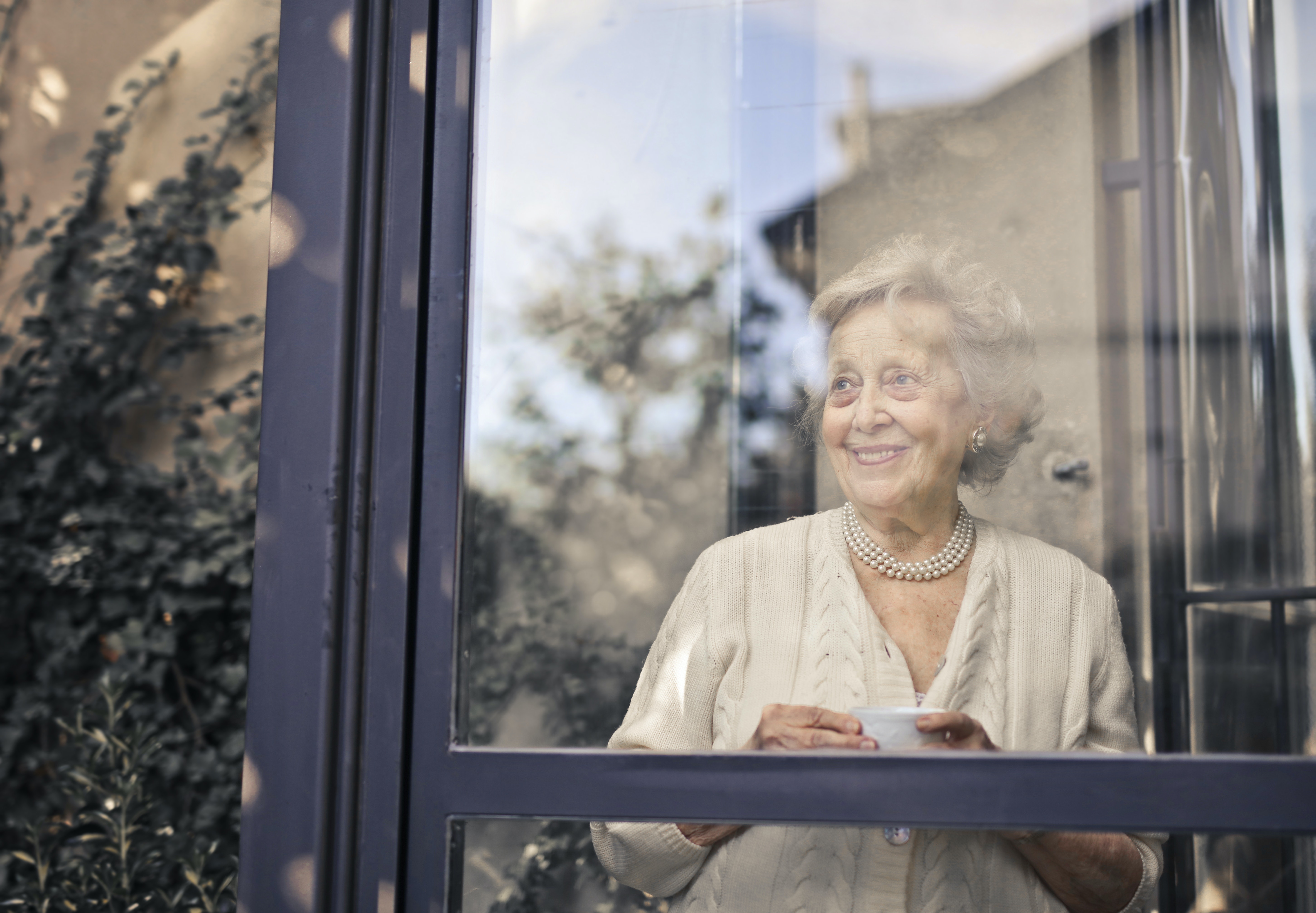 senior woman smiling out window holding tea