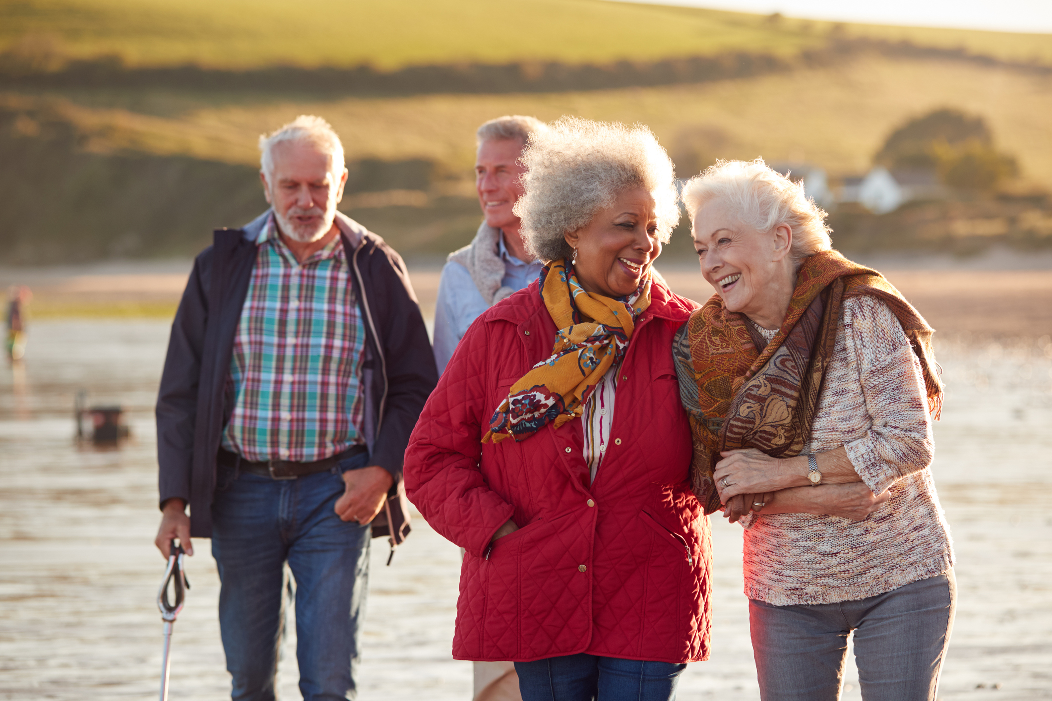 Groupe d'amis seniors souriants marchant bras dessus bras dessous le long du rivage