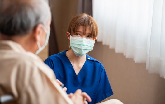 Young nurse kneeling beside older patient