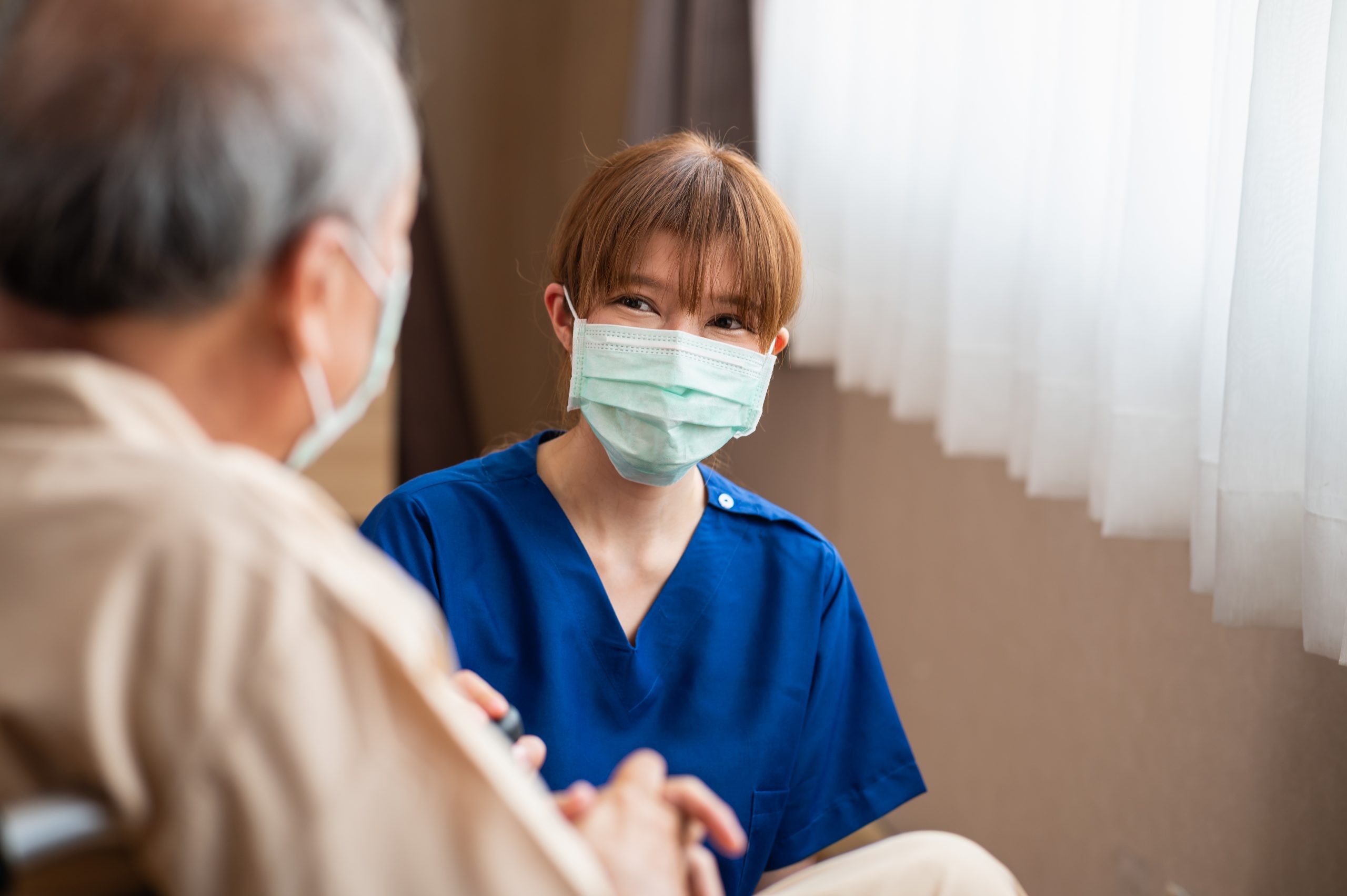 Young nurse kneeling beside older patient