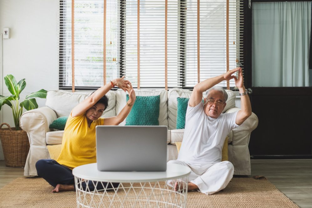 Couple de personnes âgées faisant du yoga devant un ordinateur portable
