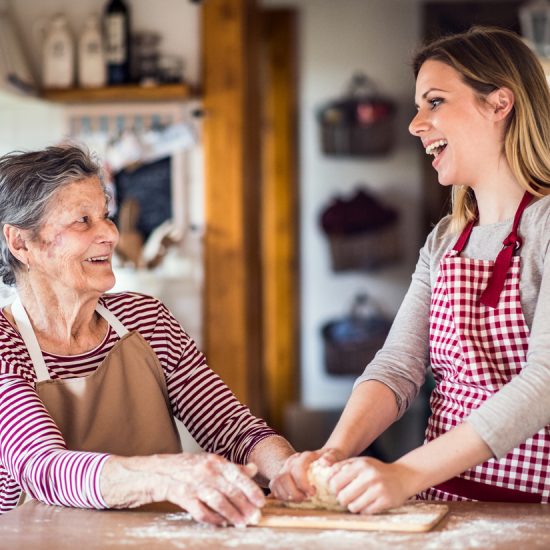 Une grand-mère âgée avec une petite-fille adulte à la maison, cuisinant