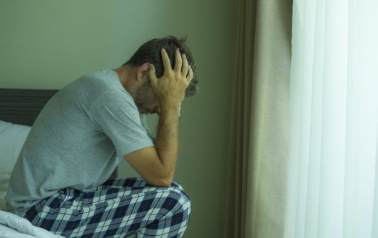 Man sitting on bed holding head in hands