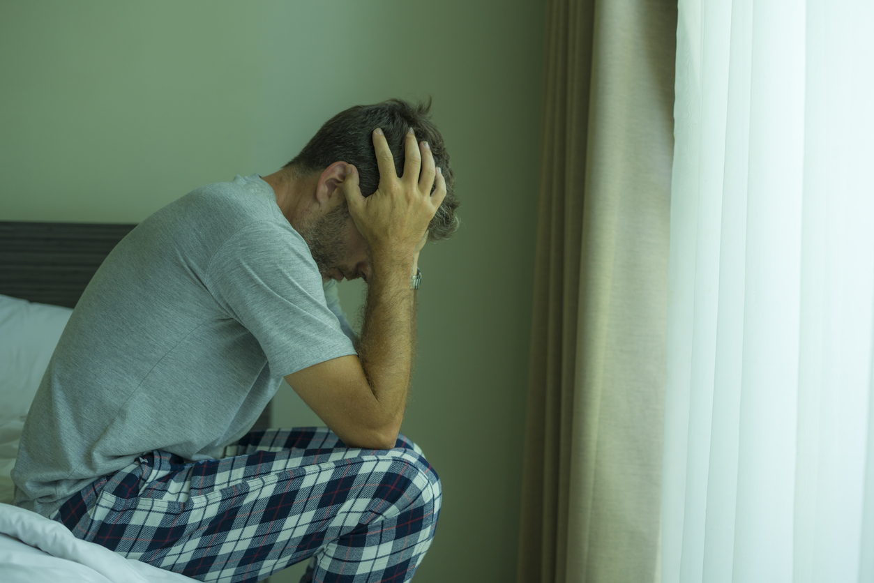 Man sitting on bed holding head in hands