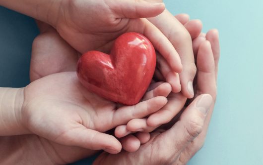 Adult and child hands holding red heart