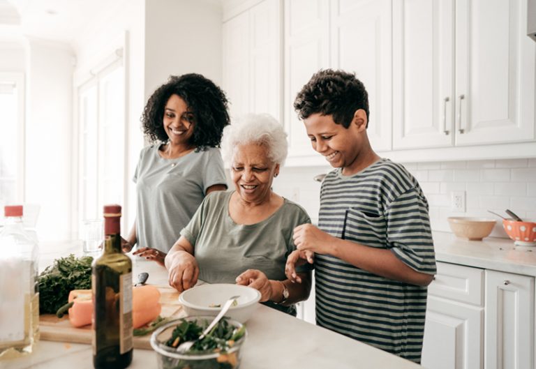 Grandmother and two children standing in the kitchen. They look happy while prepping food.