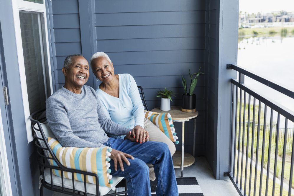Senior couple relaxing on porch, holding hand, smiling